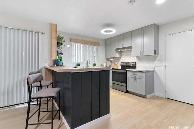 kitchen featuring electric stove, gray cabinets, light wood-type flooring, a kitchen bar, and backsplash