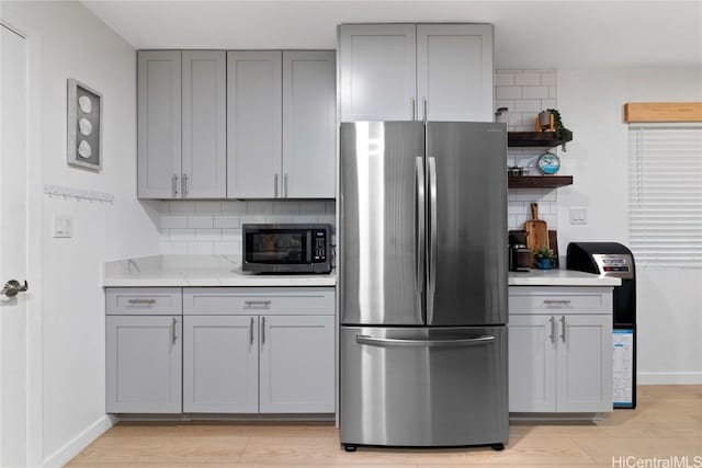 kitchen with stainless steel appliances, decorative backsplash, light stone counters, and gray cabinetry