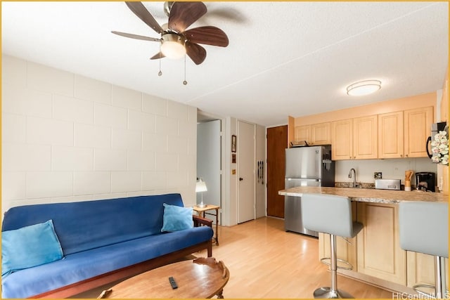 kitchen with stainless steel refrigerator, ceiling fan, sink, light hardwood / wood-style floors, and a kitchen bar