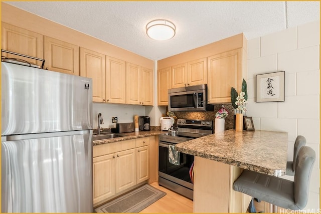 kitchen with kitchen peninsula, a breakfast bar, a textured ceiling, stainless steel appliances, and sink