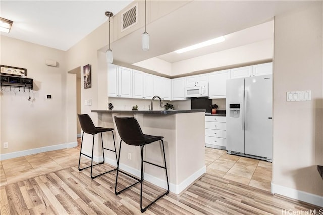 kitchen with decorative light fixtures, white cabinetry, a kitchen breakfast bar, kitchen peninsula, and white appliances