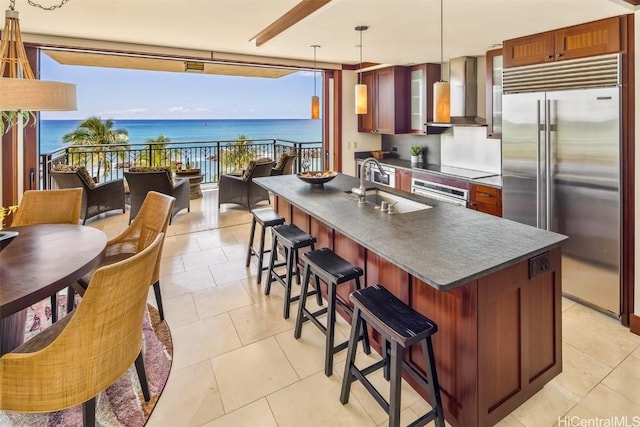 kitchen with hanging light fixtures, a water view, wall chimney range hood, appliances with stainless steel finishes, and sink