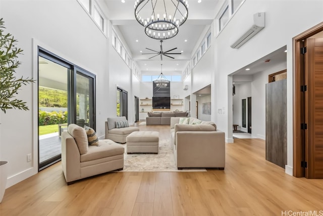 living room featuring an inviting chandelier, a towering ceiling, light hardwood / wood-style flooring, and a wall mounted AC