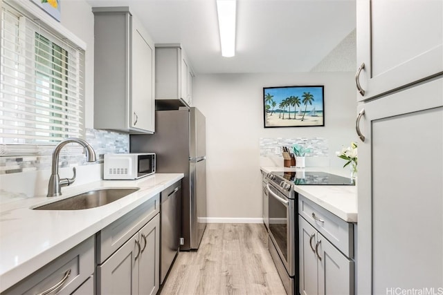 kitchen featuring decorative backsplash, sink, light hardwood / wood-style flooring, appliances with stainless steel finishes, and gray cabinetry