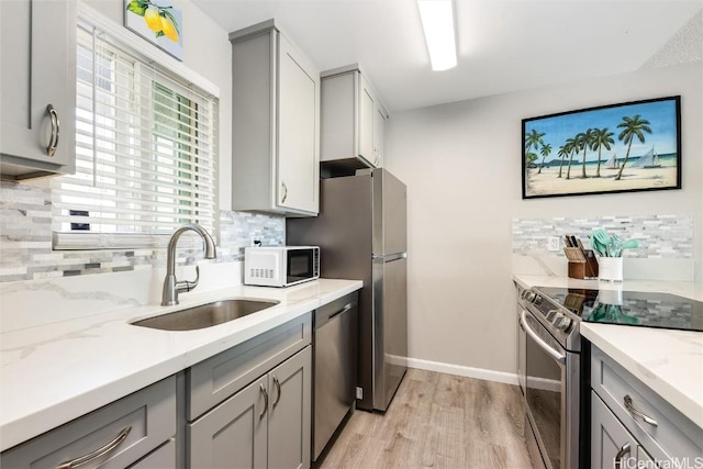 kitchen featuring gray cabinets, appliances with stainless steel finishes, light wood-type flooring, light stone countertops, and sink