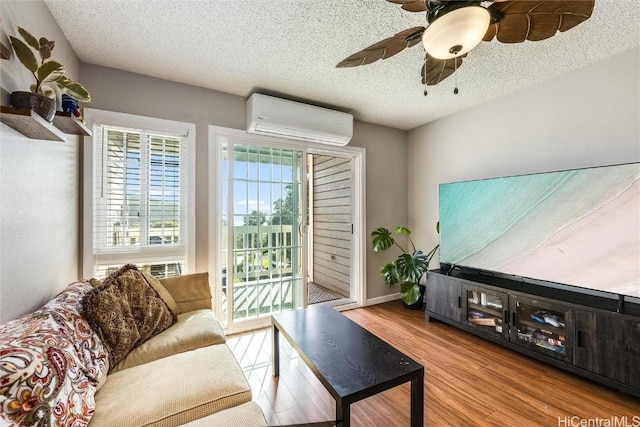 living room with ceiling fan, an AC wall unit, a textured ceiling, and light hardwood / wood-style floors