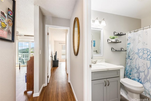 bathroom with toilet, vanity, wood-type flooring, a textured ceiling, and curtained shower