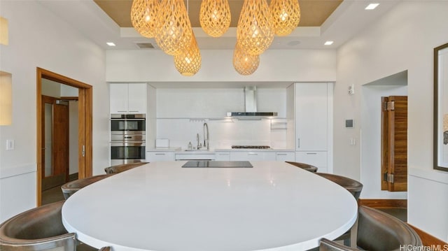 kitchen with sink, double oven, white cabinets, black electric stovetop, and wall chimney range hood