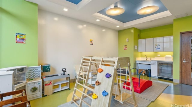 rec room with wine cooler, a tray ceiling, and indoor wet bar