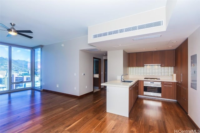 kitchen with sink, oven, dark hardwood / wood-style flooring, backsplash, and kitchen peninsula