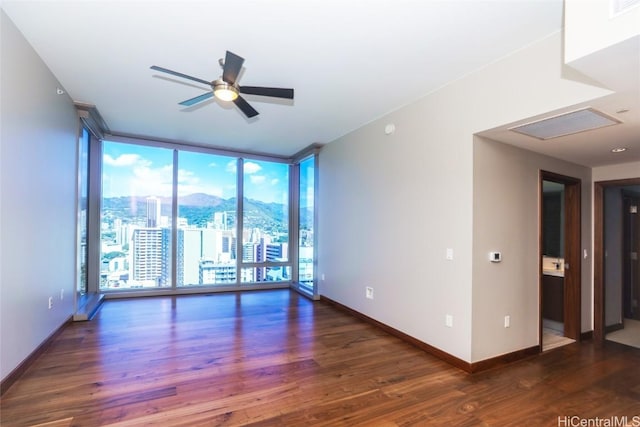 empty room featuring a mountain view, a wall of windows, dark hardwood / wood-style floors, and ceiling fan