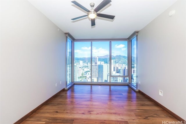 unfurnished room featuring dark hardwood / wood-style flooring, a healthy amount of sunlight, ceiling fan, and a wall of windows