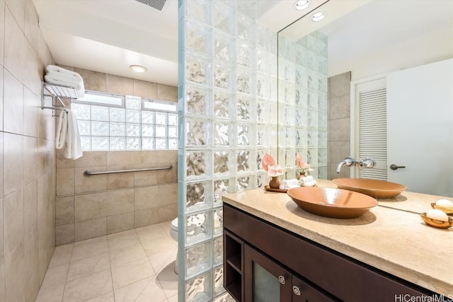 bathroom with toilet, tile patterned floors, vanity, and tile walls