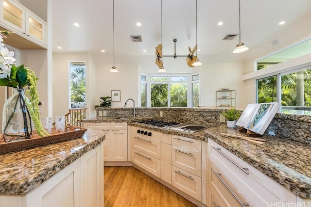 kitchen featuring pendant lighting, light hardwood / wood-style floors, stainless steel gas cooktop, white cabinets, and dark stone counters