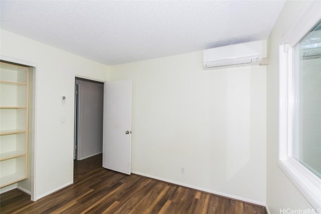 unfurnished bedroom with a textured ceiling, a closet, a wall mounted air conditioner, and dark hardwood / wood-style floors