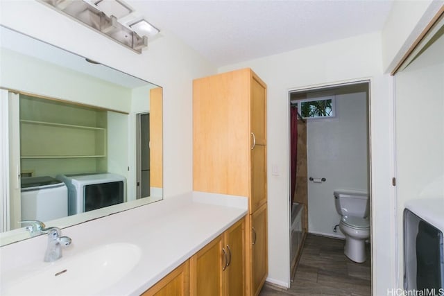 bathroom with toilet, a textured ceiling, washer and clothes dryer, a bathing tub, and vanity