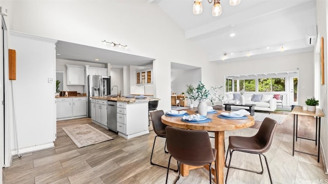 dining room featuring beam ceiling, high vaulted ceiling, rail lighting, and light wood finished floors