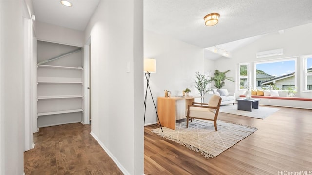 interior space with baseboards, lofted ceiling, a wall unit AC, wood finished floors, and a textured ceiling