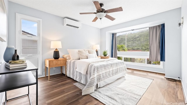 bedroom with a ceiling fan, wood finished floors, baseboards, and a wall mounted air conditioner