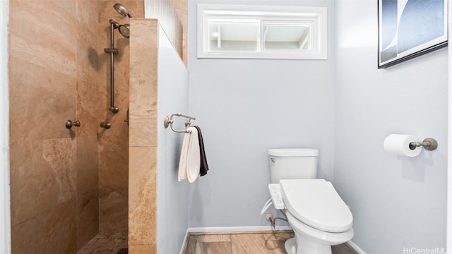 bathroom with tiled shower, toilet, baseboards, and wood finished floors