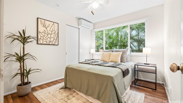 bedroom featuring wood finished floors, baseboards, ceiling fan, an AC wall unit, and a textured ceiling