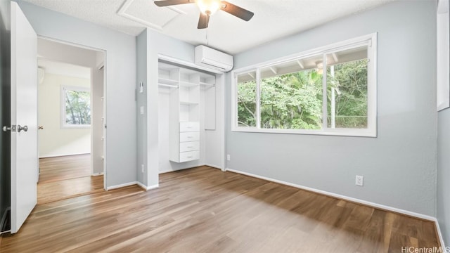 unfurnished bedroom with a wall unit AC, wood finished floors, baseboards, ceiling fan, and a closet