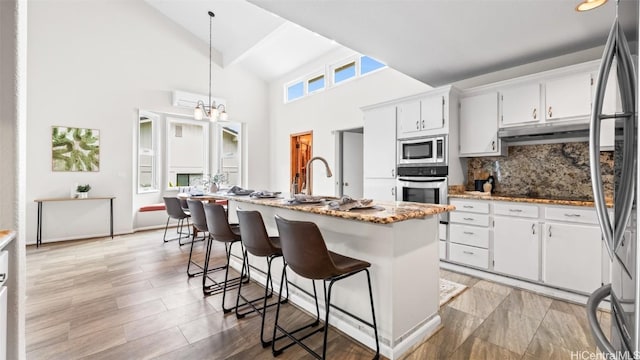 kitchen featuring under cabinet range hood, decorative backsplash, appliances with stainless steel finishes, and white cabinetry