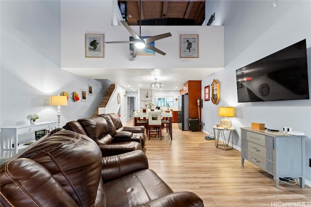 living room featuring ceiling fan, a towering ceiling, and light wood-type flooring