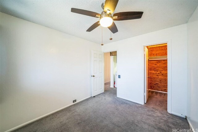 unfurnished bedroom featuring baseboards, ceiling fan, carpet, a walk in closet, and a textured ceiling