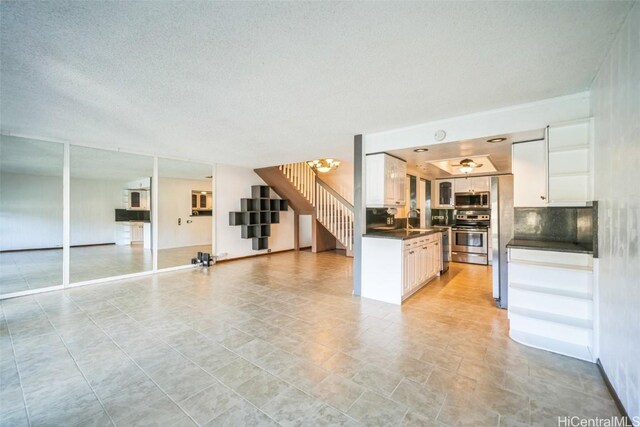 kitchen with white cabinets, dark countertops, appliances with stainless steel finishes, open floor plan, and a sink