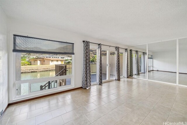 tiled spare room with a water view, a textured ceiling, and baseboards