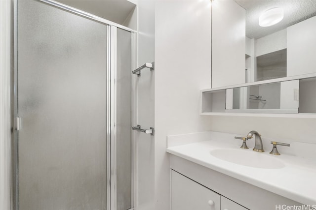 bathroom featuring a textured ceiling, a shower with door, and vanity