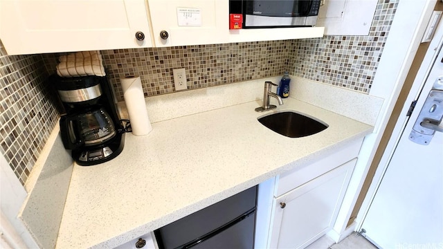 kitchen with white cabinetry, a sink, decorative backsplash, and stainless steel microwave