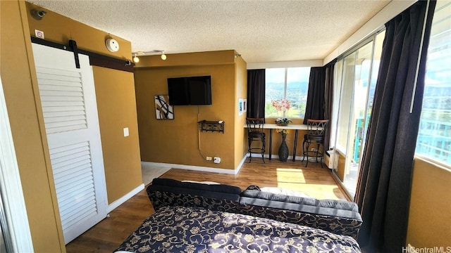 interior space with a textured ceiling, a barn door, wood finished floors, and baseboards