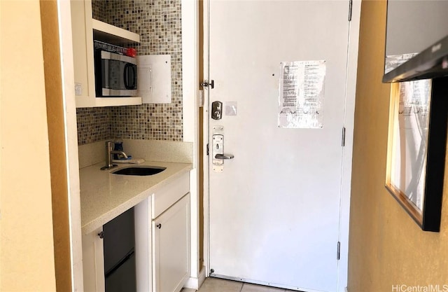 kitchen featuring a sink, white cabinetry, light countertops, tasteful backsplash, and stainless steel microwave