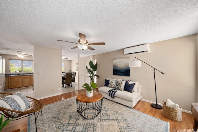 living room with an AC wall unit, light hardwood / wood-style floors, a textured ceiling, and ceiling fan