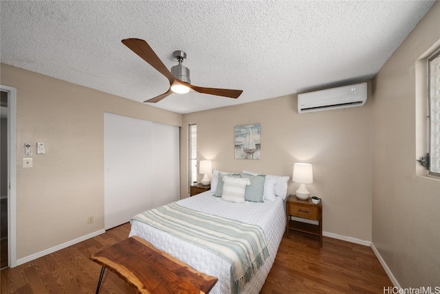 bedroom with a textured ceiling, a wall mounted AC, dark hardwood / wood-style floors, and ceiling fan