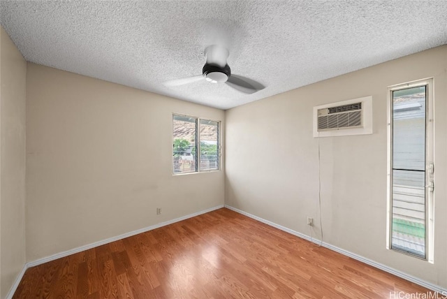 empty room featuring light hardwood / wood-style floors, a textured ceiling, a wall unit AC, and ceiling fan