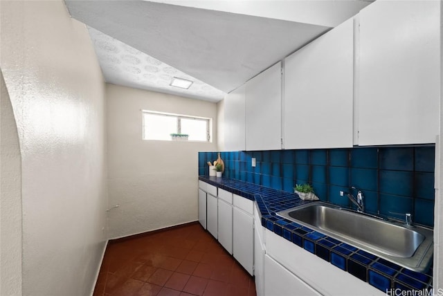 kitchen with white cabinets, dark tile patterned floors, sink, backsplash, and tile countertops