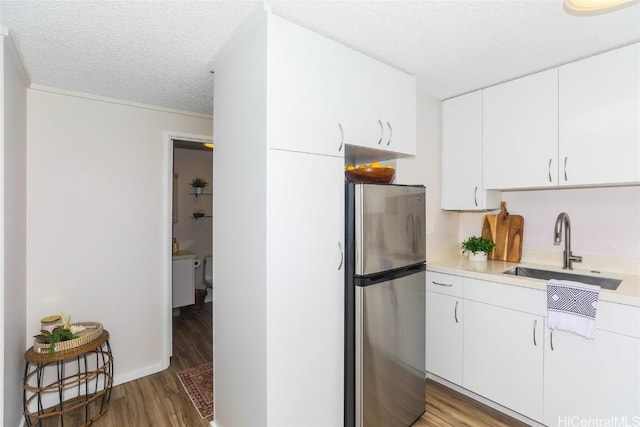 kitchen featuring light wood-type flooring, stainless steel refrigerator, a textured ceiling, white cabinets, and sink