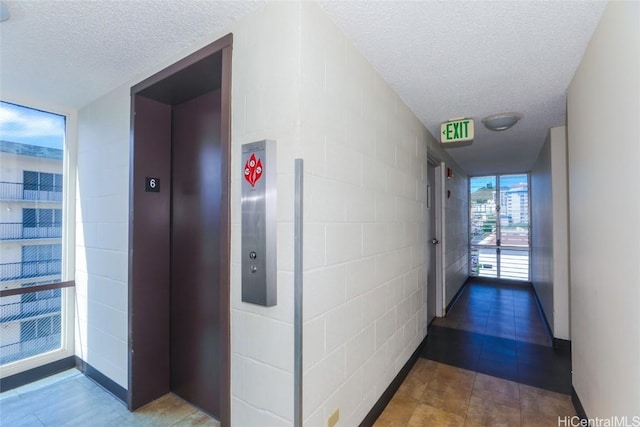 hall with a wall of windows, a textured ceiling, and elevator