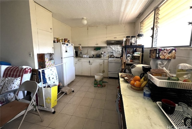 kitchen featuring white appliances, white cabinets, light tile patterned flooring, and a textured ceiling