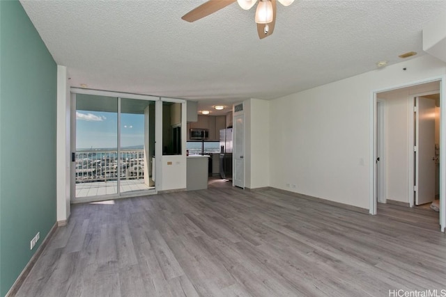 unfurnished living room with ceiling fan, a wall of windows, light wood-type flooring, and a textured ceiling