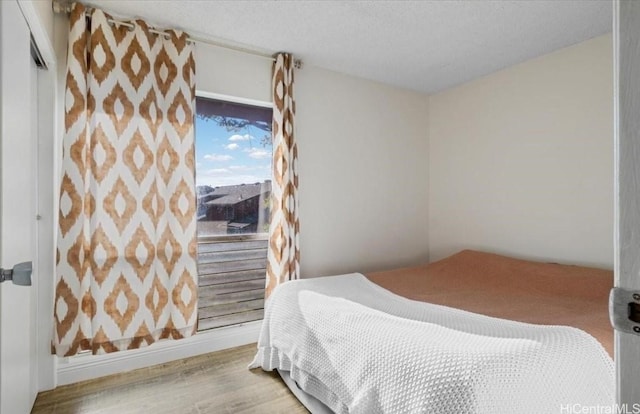 bedroom with a textured ceiling, baseboards, and wood finished floors