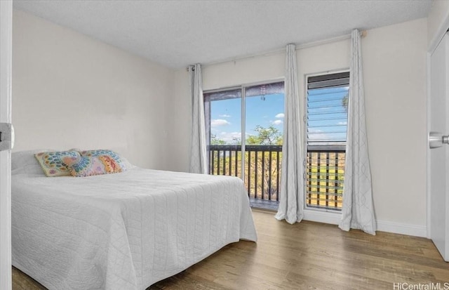 bedroom featuring a textured ceiling, baseboards, wood finished floors, and access to exterior