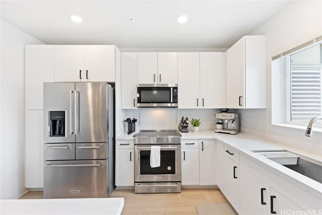 kitchen featuring appliances with stainless steel finishes, light hardwood / wood-style flooring, white cabinets, and sink