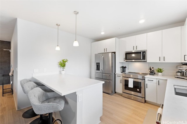 kitchen with decorative light fixtures, white cabinets, kitchen peninsula, stainless steel appliances, and light hardwood / wood-style flooring