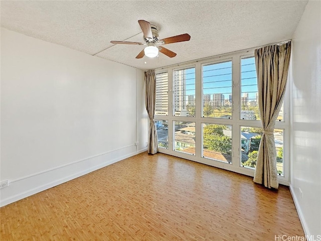 unfurnished room featuring ceiling fan, hardwood / wood-style flooring, a textured ceiling, and a wall of windows