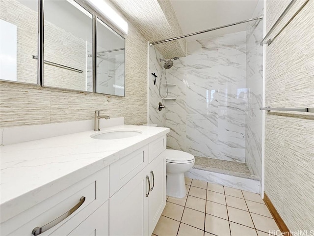 bathroom with toilet, vanity, a tile shower, and tile patterned flooring