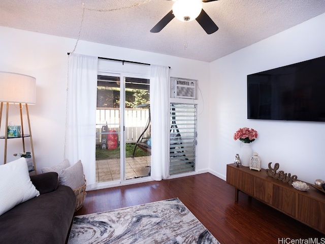 living room with a wall mounted AC, a textured ceiling, ceiling fan, and dark wood-type flooring